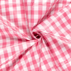 Könnte beinhalten: Rosa-weißes Gingham-Gewebe mit glänzender Oberfläche. Der Stoff ist gefaltet und verdreht, wodurch die Textur und das Muster sichtbar werden.