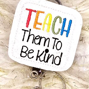 May include: White square badge holder with a rainbow colored "TEACH" and the text "Them to Be Kind" in black. The badge holder is attached to a silver swivel clip.