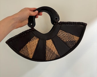 May include: A fan-shaped handbag with a dark brown leather handle and trim. The body of the bag features alternating panels of dark brown leather and woven tan material, creating a unique texture and design.