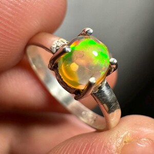 Puede incluir: Un anillo de plata con una piedra preciosa de ópalo verde y amarillo engastada en garras.