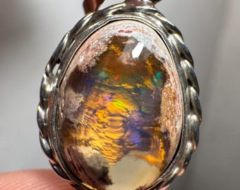 May include: A silver pendant with a large, oval-shaped opal gemstone. The opal has a white base with flashes of yellow, orange, green, and blue.