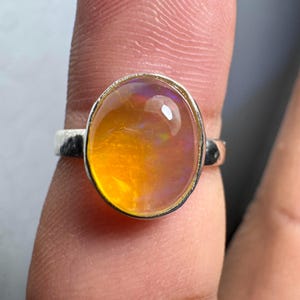 Puede incluir: Un anillo de plata con una gran piedra de ópalo ovalada. El ópalo es de un amarillo vibrante con destellos de púrpura y rosa.