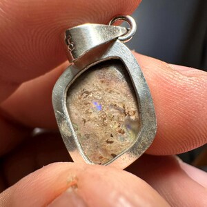 May include: A silver pendant with a light brown opal stone set in a silver frame. The pendant has a silver bail for attaching a chain.