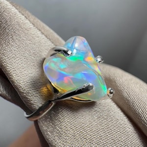 May include: A silver ring featuring a large, iridescent opal gemstone. The opal is set in a distinctive, claw-like setting.