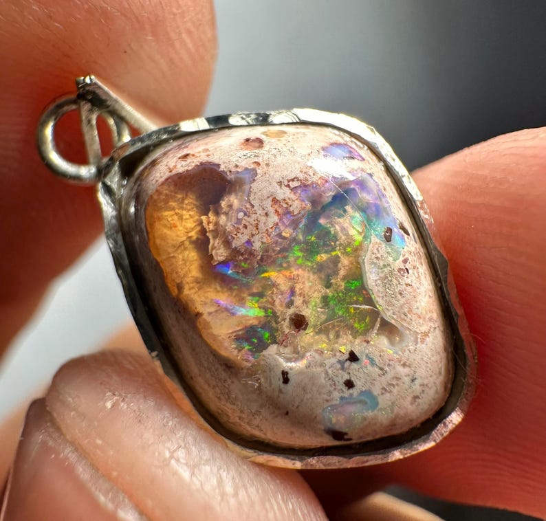 May include: A silver pendant with a light brown, white, and iridescent opal stone. The stone has a rough, textured surface and is set in a silver bezel.