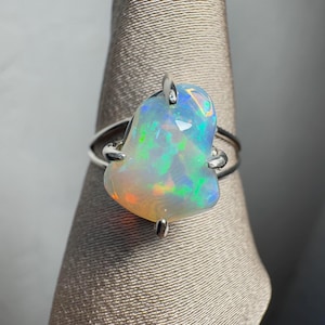 May include: A silver ring featuring a large, iridescent opal gemstone. The opal is set in a simple, claw-style setting.