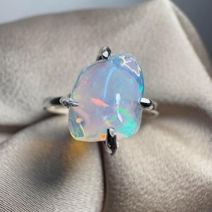 May include: A silver ring featuring a large, iridescent opal gemstone set in a claw setting.