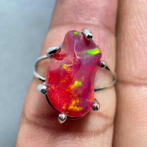 May include: A silver ring featuring a large, irregularly shaped, red and yellow opal gemstone. The opal has a bright, iridescent shine.