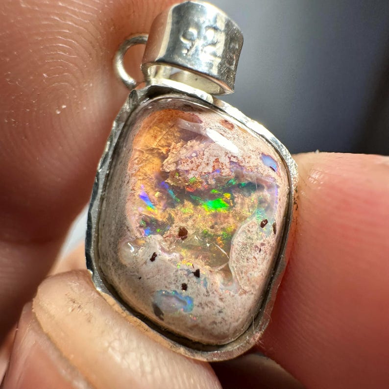 May include: A silver pendant with a light brown, white, and iridescent opal stone. The opal has a green, blue, and red flash.
