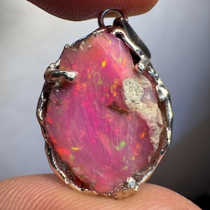 May include: A pink opal pendant with a silver setting. The opal has a rough, natural shape and is set in a silver frame with a bail for attaching a chain.