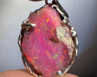 May include: A pink opal pendant with a silver setting. The opal has a rough, natural shape and is set in a silver frame with a bail for attaching a chain.