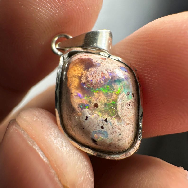 May include: A silver pendant with a pink, white, and green opal stone. The stone has a rough, natural texture and is set in a silver bezel.