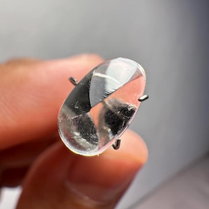 Puede incluir: Un cristal transparente de forma ovalada con un ligero brillo. El cristal está sujeto por una punta de metal.