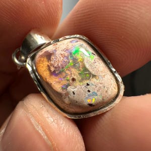 May include: A silver pendant with a light brown, white, and green opal stone. The opal has a rough, textured surface and displays iridescent colors.