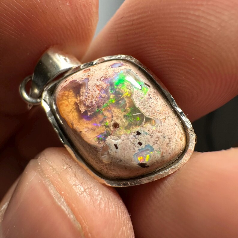 May include: A silver pendant with a light brown, white, and green opal stone. The opal has a rough, textured surface and displays iridescent colors.
