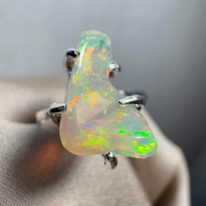 May include: A white opal ring with a silver setting. The opal has a green, yellow, and orange play of colour.