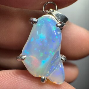 May include: A silver pendant featuring a light blue opal with iridescent flashes of green and blue. The opal is set in a silver bezel with four prongs.