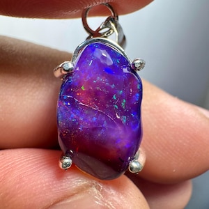 May include: A purple opal pendant with a silver setting. The opal has a vibrant purple hue with flashes of blue and green.