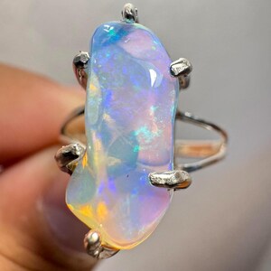 May include: A silver ring featuring a large, iridescent opal gemstone. The opal is set in a prong setting and has a unique, freeform shape.