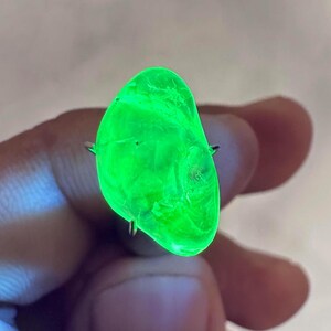 Puede incluir: Una piedra translúcida de forma irregular, de color verde brillante, con una superficie lisa. La piedra se mantiene en su lugar mediante dos clavijas metálicas.