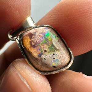 May include: A silver pendant with a large, irregular-shaped opal stone. The opal has a white base with flashes of green, blue, and orange.
