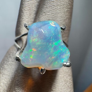 May include: A silver ring featuring a large, light blue opal gemstone. The opal has an irregular shape and shows flashes of green and orange.