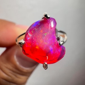 May include: A silver ring featuring a large, freeform, red and purple opal gemstone. The opal has a high shine and is set in a simple, modern design.