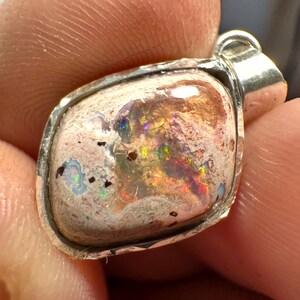 May include: A silver pendant featuring a white opal with iridescent flashes of blue, green, and red. The opal is set in a silver bezel.
