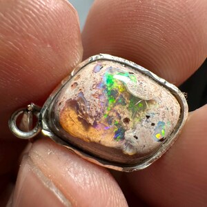May include: A silver pendant with a white opal stone set in a textured silver bezel. The opal has a rainbow of colors, including green, blue, and purple.