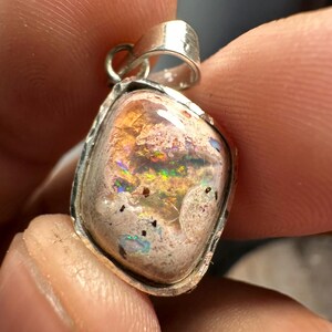 May include: A silver pendant with a light pink opal stone. The opal has a variety of colors, including orange, green, and blue.