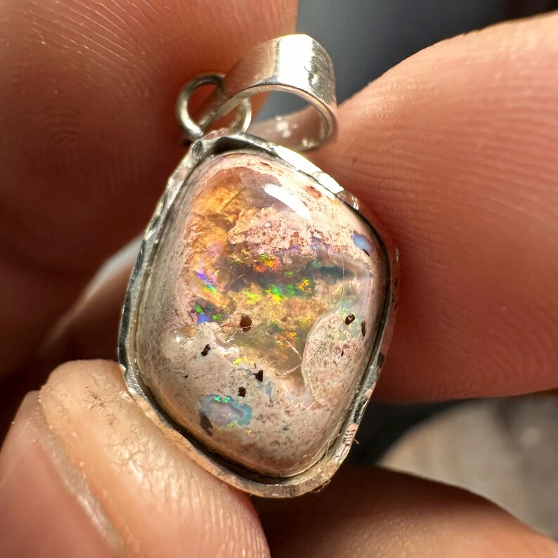 May include: A silver pendant with a light pink opal stone. The opal has a variety of colors, including orange, green, and blue.