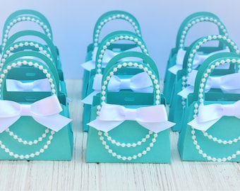 Op de afbeelding: Tealblauwe en witte cadeaudoosjes in de vorm van handtassen met parelranden en witte satijnen strikken.