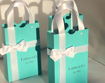 May include: Several small, rectangular gift bags in a light blue color, with white ribbon handles and bows. The bags have a vertical white stripe and the text "LARISSA & Co. Est. 2003" printed on the front.
