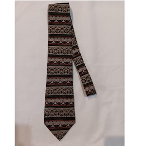 May include: A patterned necktie with a repeating design of ornate shapes and swirls in shades of black, brown, red, and blue. The tie is displayed on a white surface.