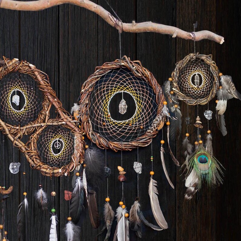 May include: A wall hanging featuring three circular woven branch hoops suspended from a horizontal wooden branch. Each hoop contains a black web with a central clear crystal, adorned with hanging feathers, beads, and a peacock eye feather.