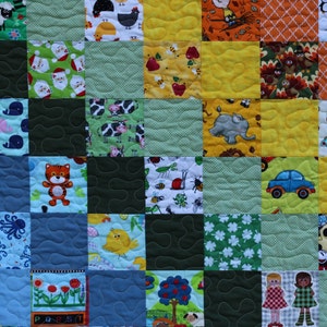 Puede incluir: Una colcha de retazos colorida con varios dise&ntilde;os, incluyendo animales, letras y un coche. La colcha est&aacute; hecha de cuadrados de diferentes telas y colores, incluyendo azul, verde, amarillo y rojo.