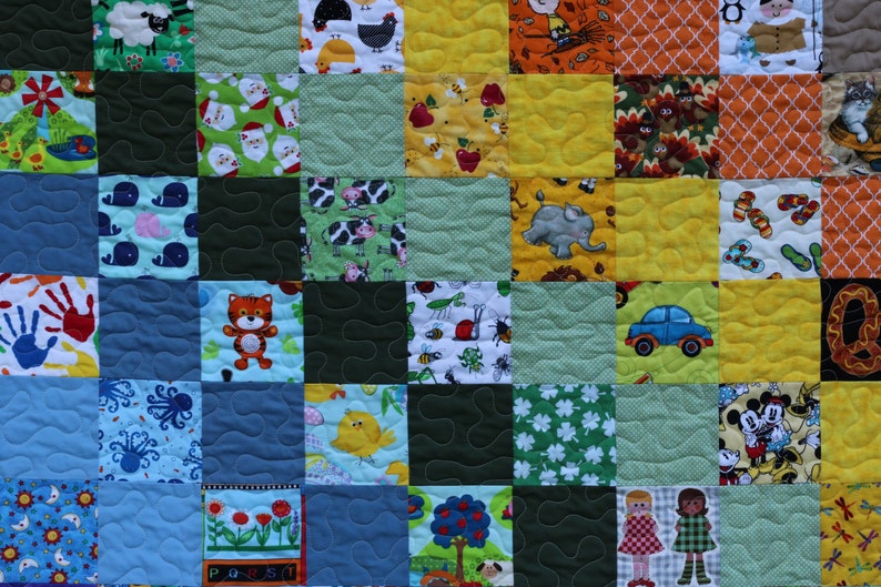 Puede incluir: Una colcha de retazos colorida con varios dise&ntilde;os, incluyendo animales, letras y un coche. La colcha est&aacute; hecha de cuadrados de diferentes telas y colores, incluyendo azul, verde, amarillo y rojo.