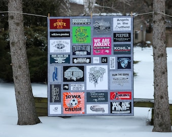 Puede incluir: Una colcha gris y blanca hecha de camisetas con varios logotipos y textos, incluyendo "Centennial Soccer", "Endless Elmmer", "We Are Ankeny", "Jaguars", "Dome Bound", "Own The Game", "Ankeny", y "We Are One".