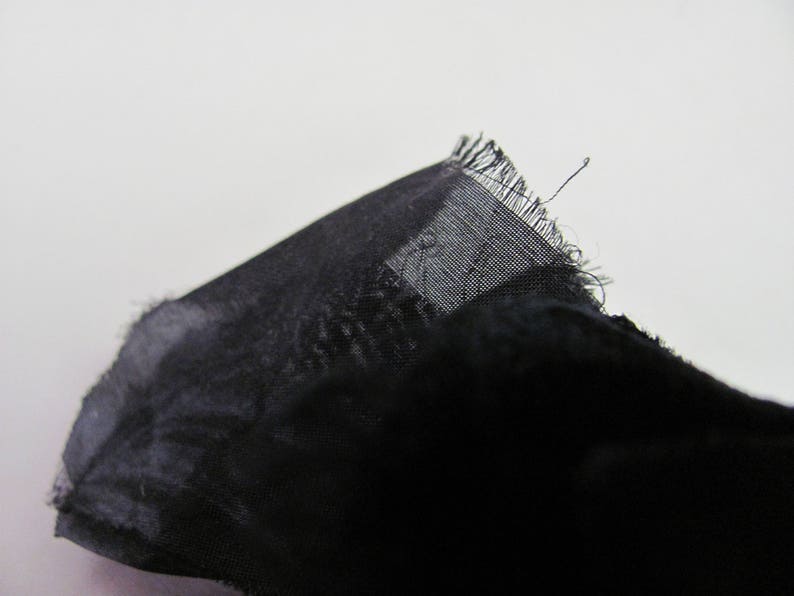 May include: Black sheer fabric with a frayed edge.