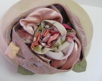 May include: A pink and white fabric rose with a pearl accent, attached to a beige felt hat.