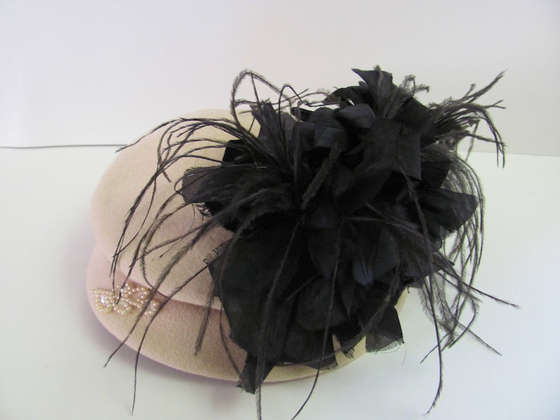 May include: A beige felt hat with a black feather and flower embellishment.