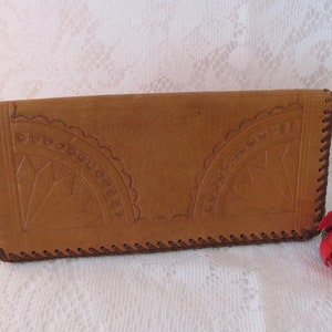 May include: A brown leather wallet with intricate embossed designs and a brown stitched border.