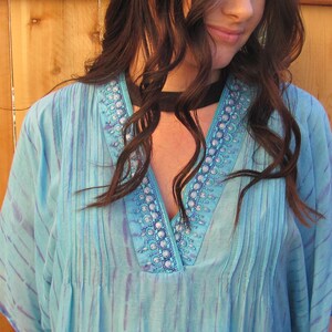 May include: A light blue, sheer, embroidered top with a V-neckline and a black choker necklace.