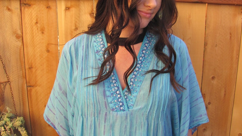 May include: A light blue, sheer, embroidered top with a V-neckline and a black choker necklace.