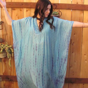 May include: A light blue tie-dye kaftan with a beaded neckline. The kaftan is made of a soft, flowing fabric and has a relaxed fit.