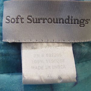 May include: A white tag with the text "Soft Surroundings" in black lettering. The tag is attached to a teal fabric with a white and blue pattern.