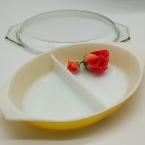 May include: A yellow divided baking dish with a clear glass lid. The dish is divided into two sections and has a white interior. Two small red roses are placed on top of the dish.