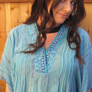 May include: A blue and purple tie-dye kaftan with a beaded neckline. The kaftan has a V-neck and short sleeves.