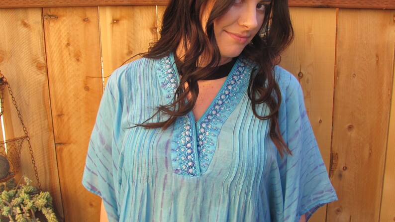 May include: A blue and purple tie-dye kaftan with a beaded neckline. The kaftan has a V-neck and short sleeves.