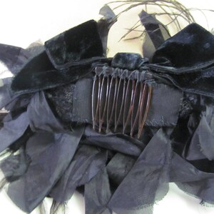 May include: A black velvet hair comb with a black feather and ribbon embellishment. The comb is decorated with a large black bow and a black feather.
